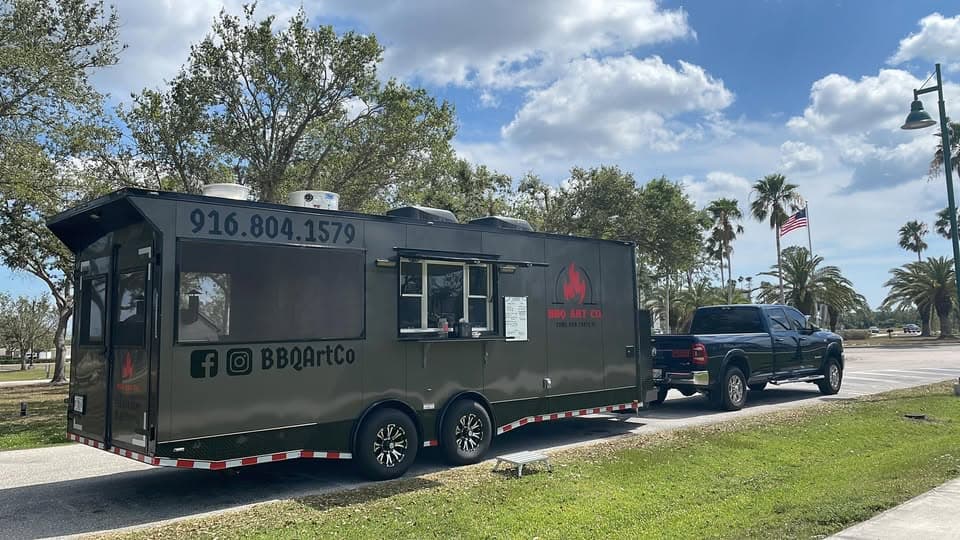 BBQ Art Co. food truck and trailer parked under Florida palms