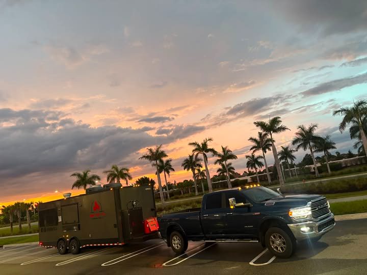 BBQ Art Co. trailer hitched to the pickup truck in a parking lot at sunset, palm trees behind